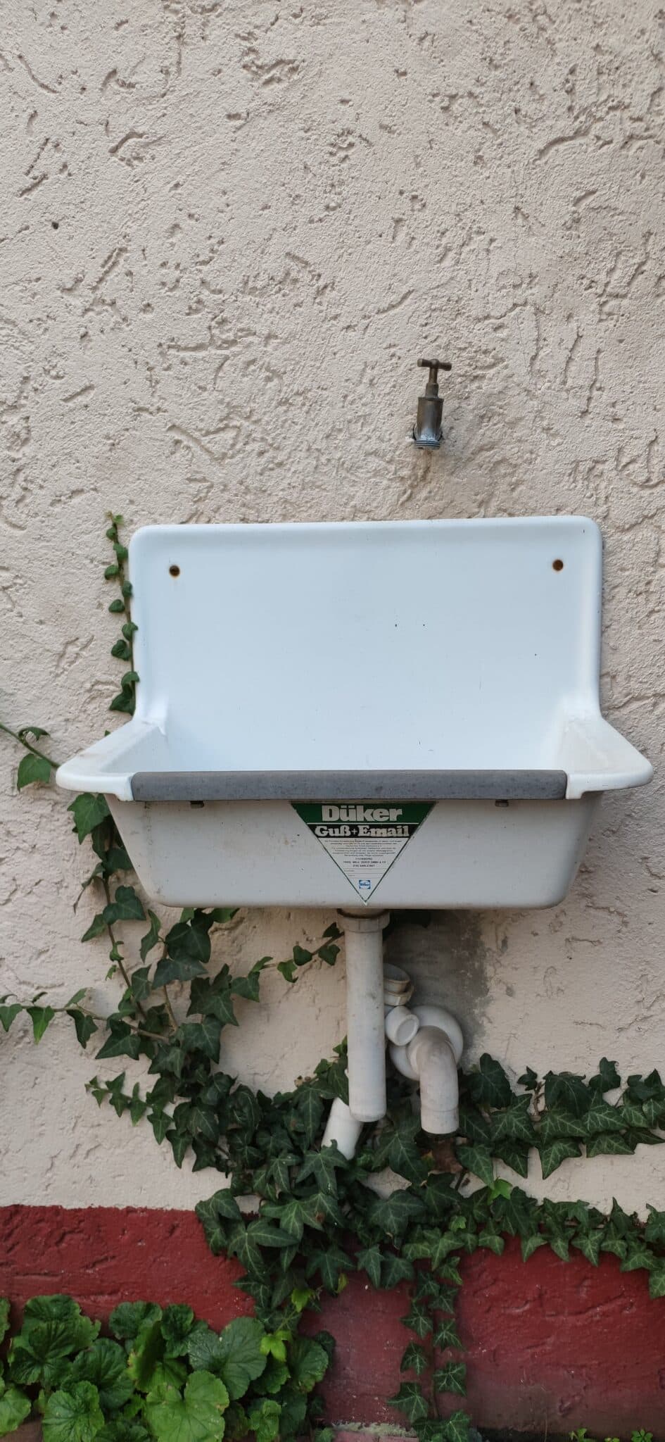 Wandwaschbecken mit schlichter Form, bepflanzt mit Efeu, an einer strukturierten Wand montiert.