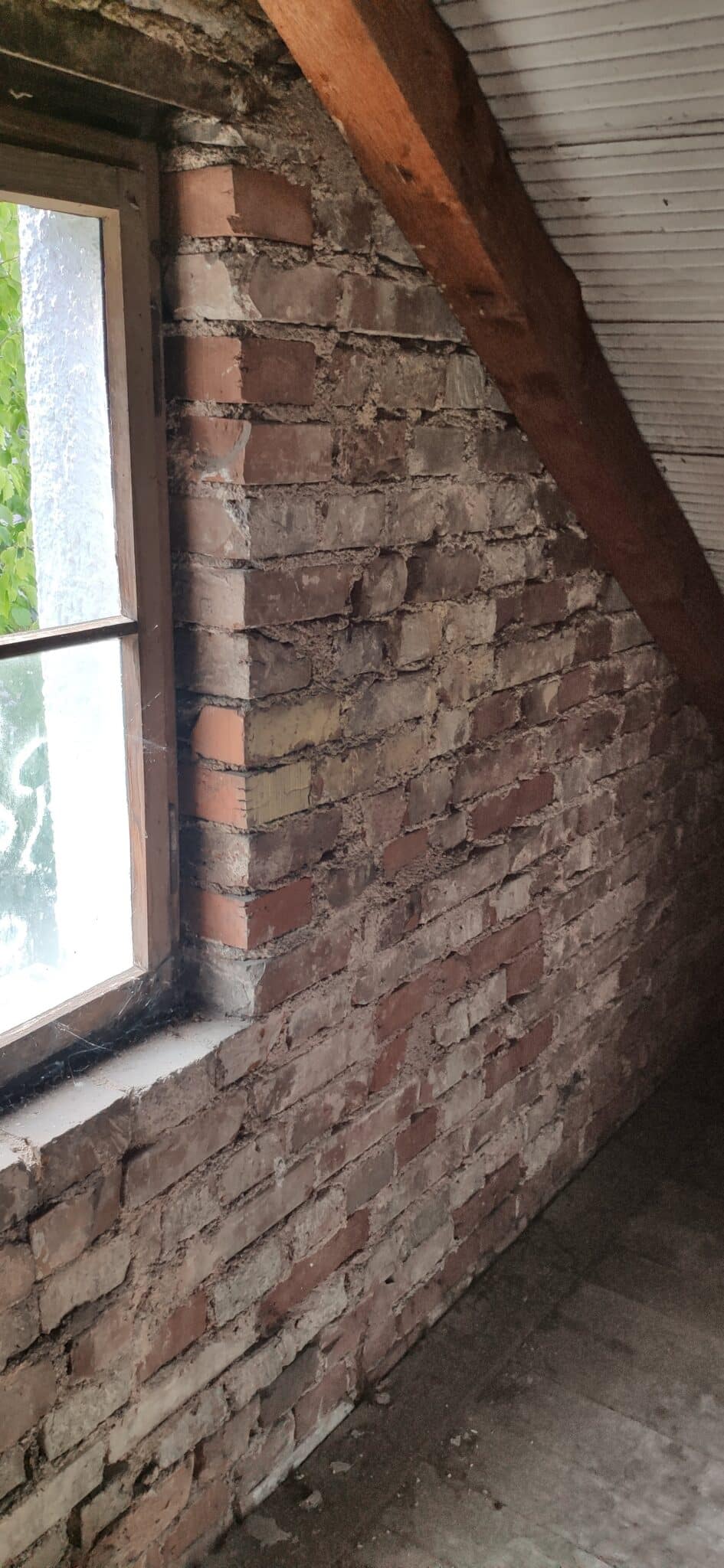 Ein gemauerter Innenraum mit einer Fensteröffnung, sichtbar sind Ziegelsteine und Putzreste unter einer schräge Decke.