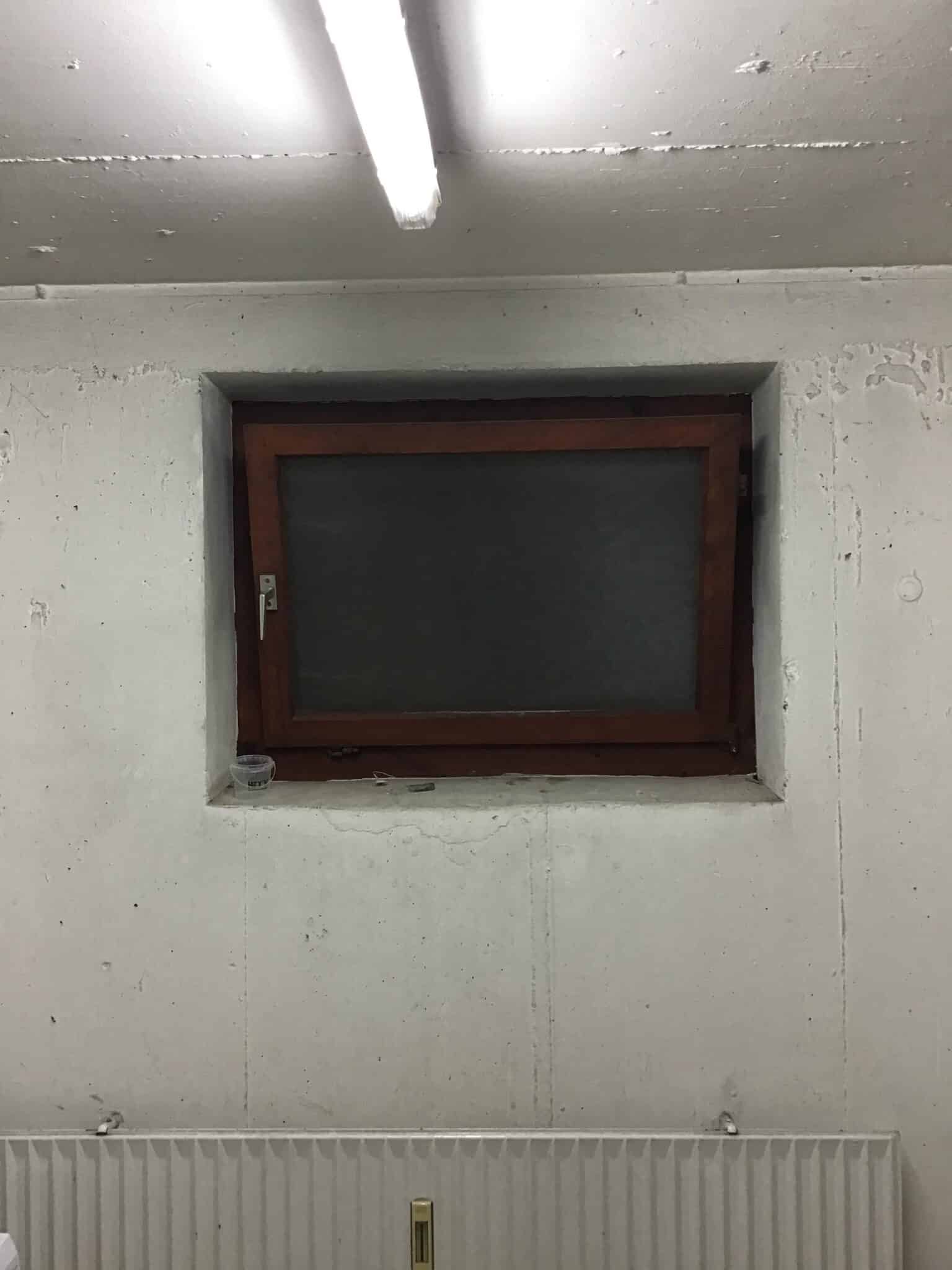 Fenster in einer grauen Wand mit sichtbarer Betonstruktur und Heizkörper darunter.
