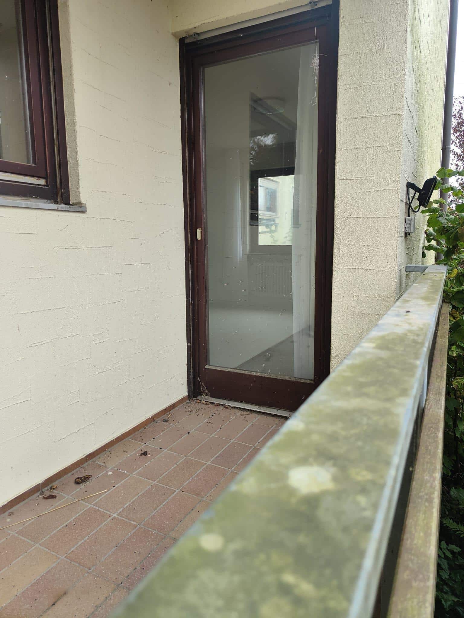 Ein leerer Balkon mit einer Tür, die zum Innenraum führt, und einem balustradenartigen Geländer.