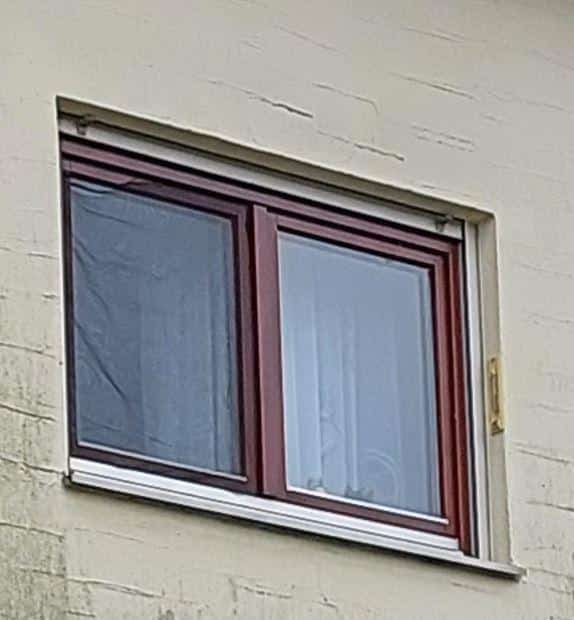 Fenster mit rotem Rahmen in einer hellen Wand, leicht geöffnet, mit Vorhängen im Inneren.
