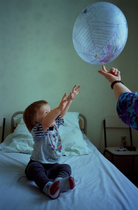 Ein Kind sitzt auf einem Bett und spielt mit einem Luftballon.