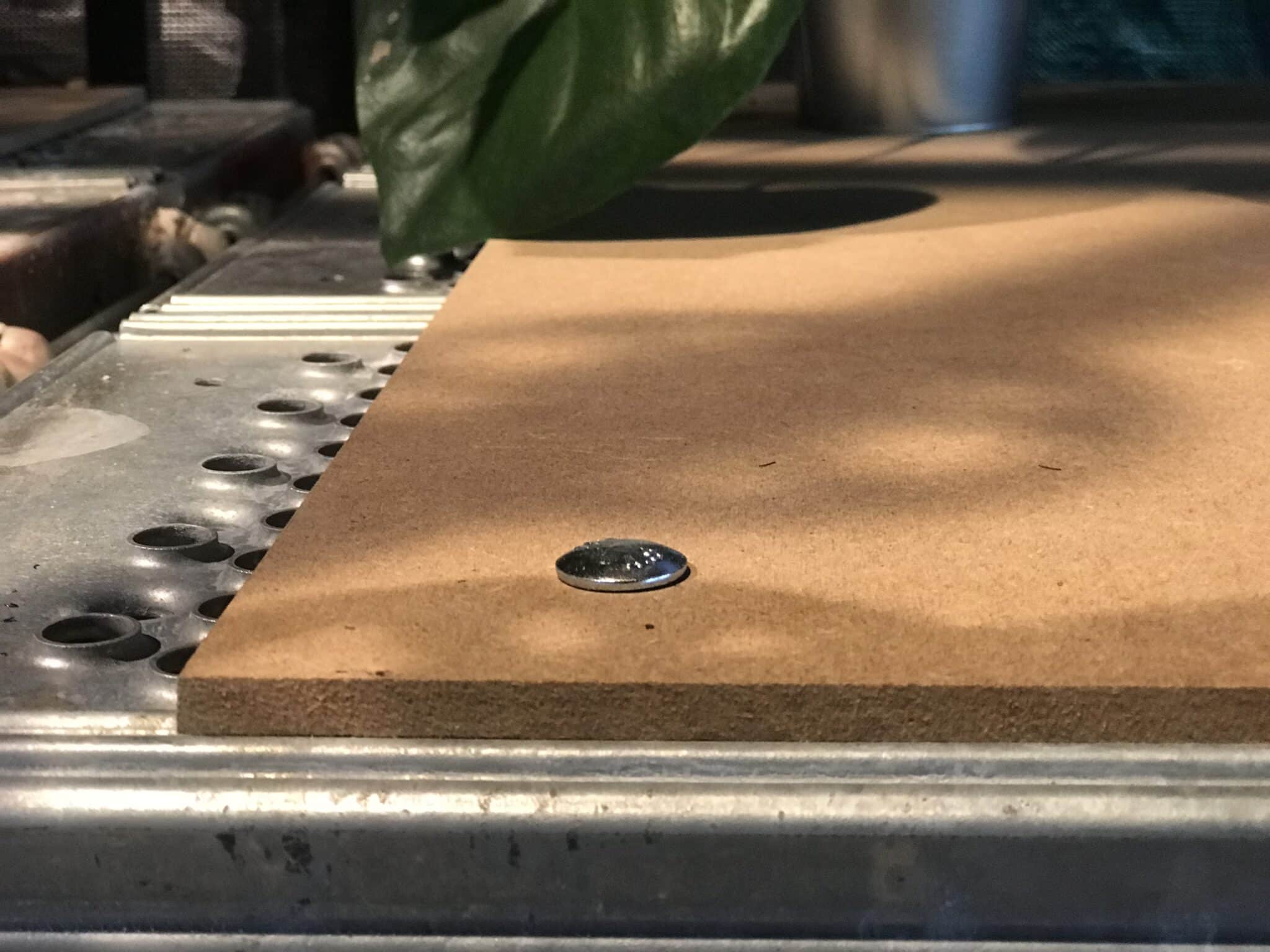 Eine MDF-Platte liegt auf einem Metallgestell, ein Schraubenkopf ist sichtbar, daneben eine Pflanze.
