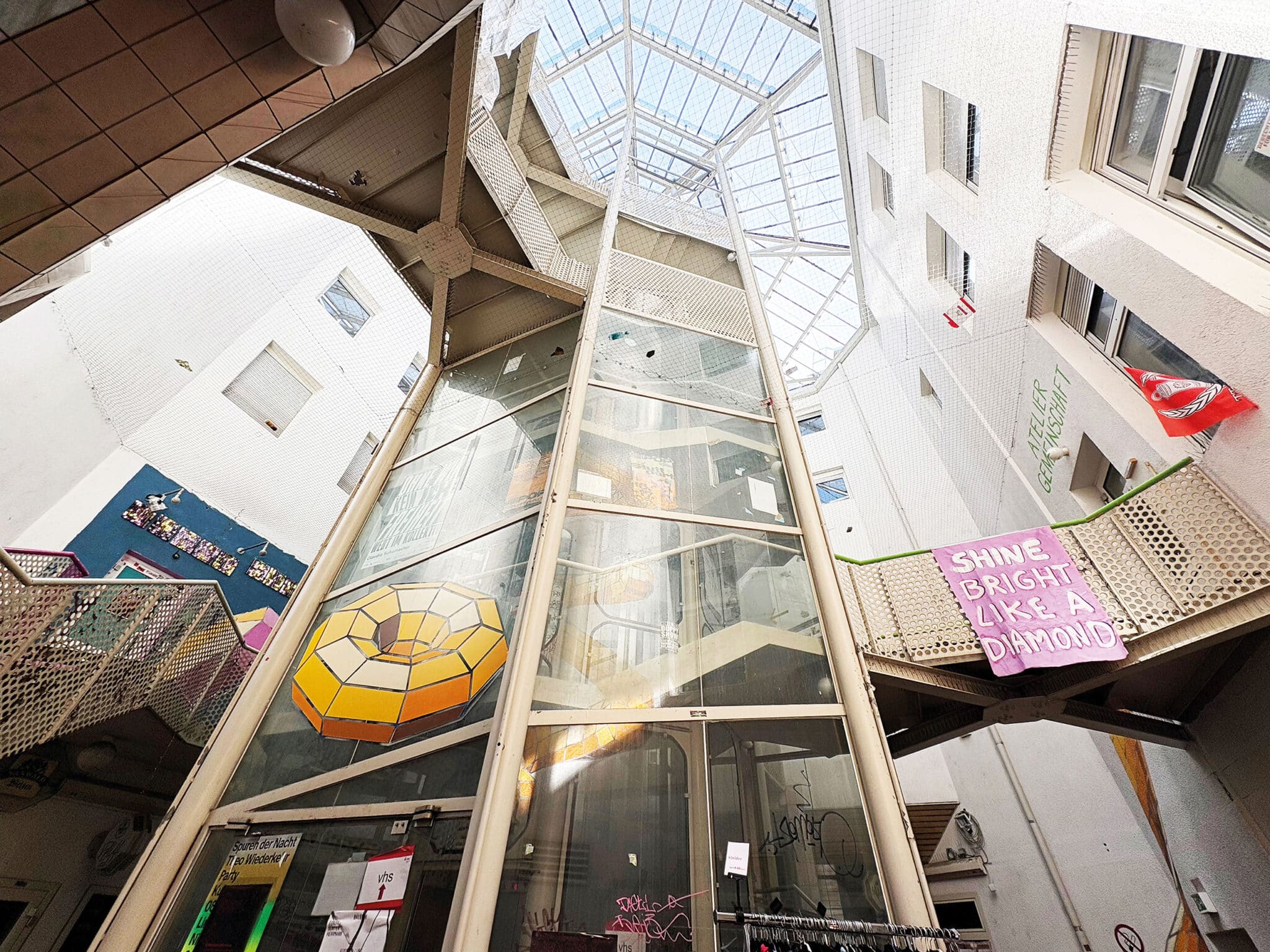 Blick in einen modernen Innenhof mit Glasaufzug und bunten Wandkunstwerken.